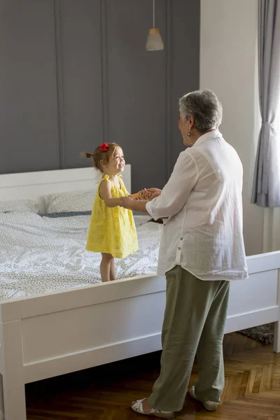 Oma spielt mit einer kleinen Enkelin auf dem Bett — Stockfoto