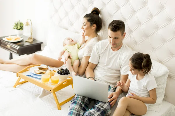 Junge Familie mit Laptop im Bett — Stockfoto