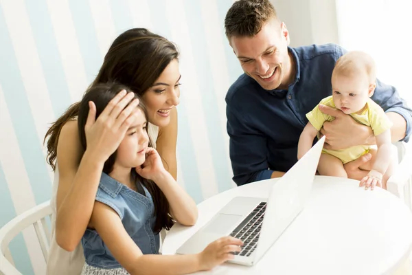Giovani genitori con figlie al tavolo con laptop — Foto Stock