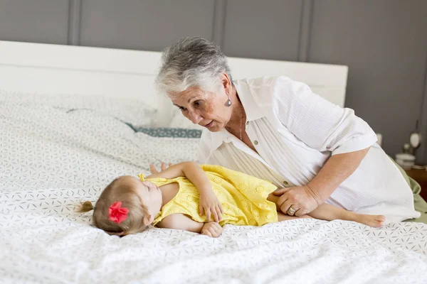 Бабушка играет с маленькой внучкой на кровати — стоковое фото