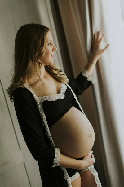 Unga gravid kvinna som står vid fönstret — Stockfoto