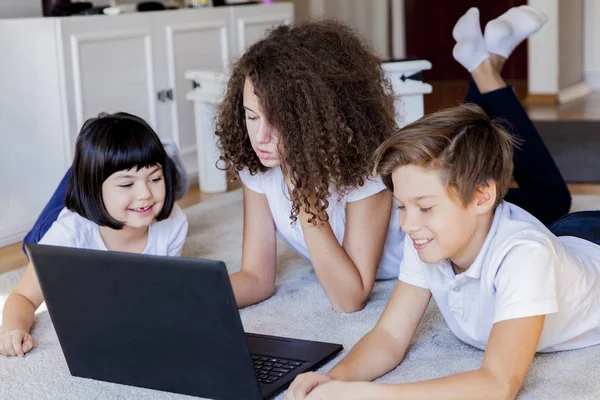 Klein meisje, tiener jongen en meisje liggend op de vloer rond laptop — Stockfoto