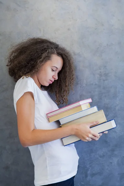 Девочка-подросток стоит у стены и держит несколько книг — стоковое фото