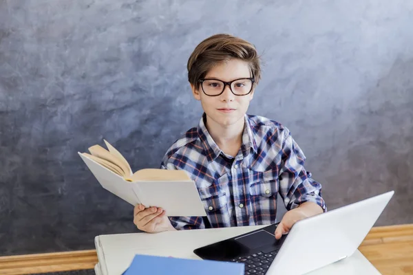 Хлопчик-підліток читає книгу і використовує ноутбук у кімнаті — стокове фото