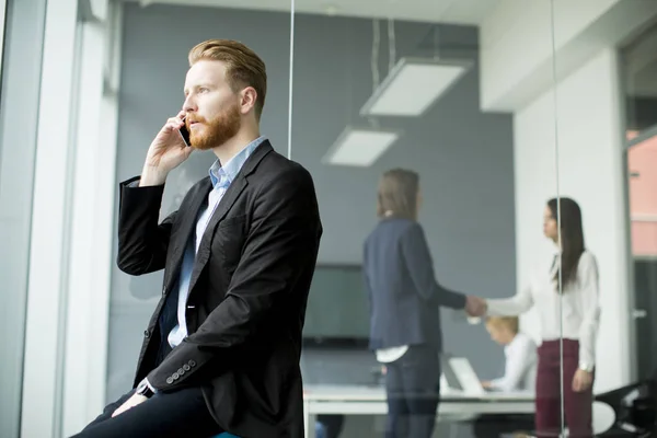 Uomo d'affari con i capelli zenzero utilizzando il telefono cellulare mentre altri busi — Foto Stock