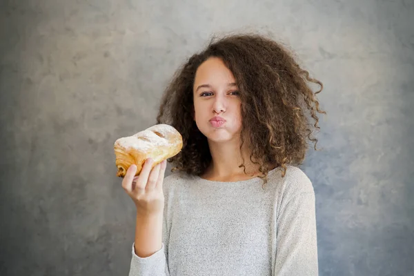 Curar chica pelo rizado comer croissant contra la pared — Foto de Stock