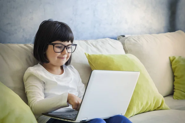 Gadis kecil berambut hitam berkacamata menggunakan laptopnya — Stok Foto