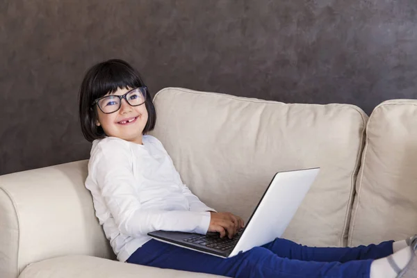 Smiling little girl with glasses using her laptop — Stock Photo, Image
