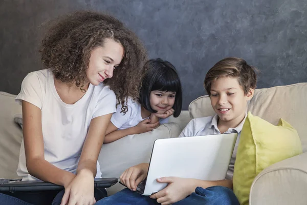 Kleines Mädchen, jugendlicher Junge und lockiges Mädchen mit Laptop auf dem Sofa — Stockfoto