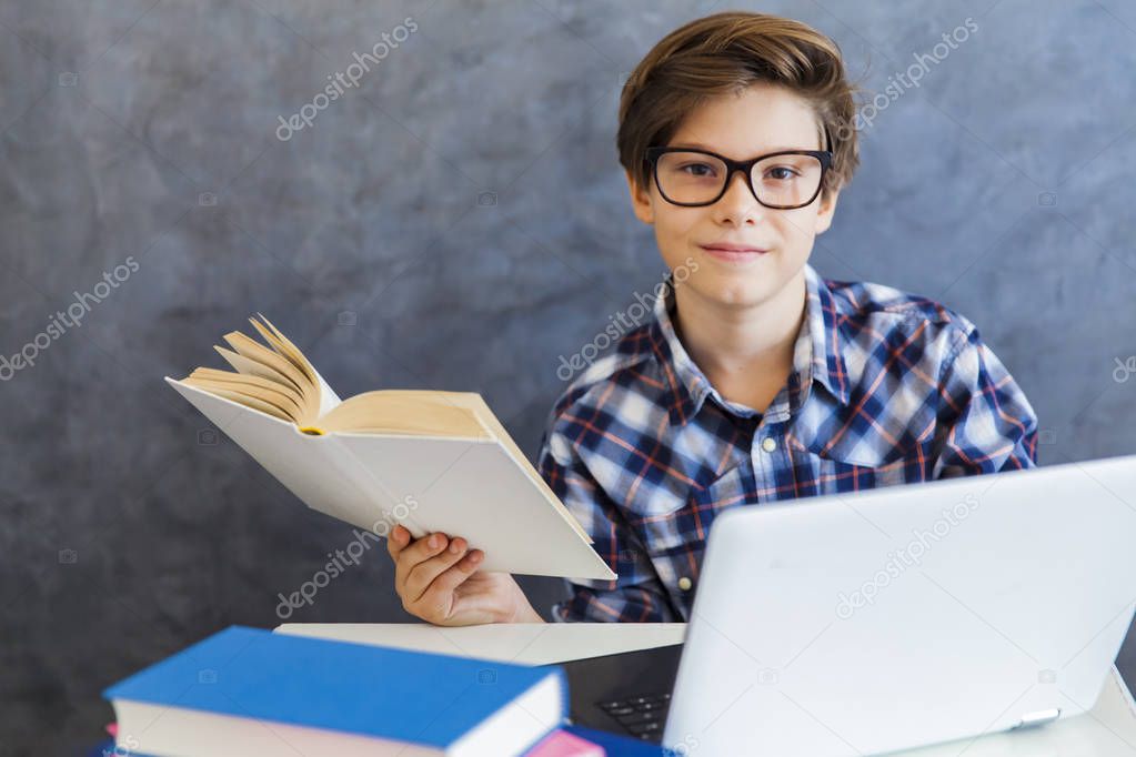 Teen boy reading book and use laptop at home