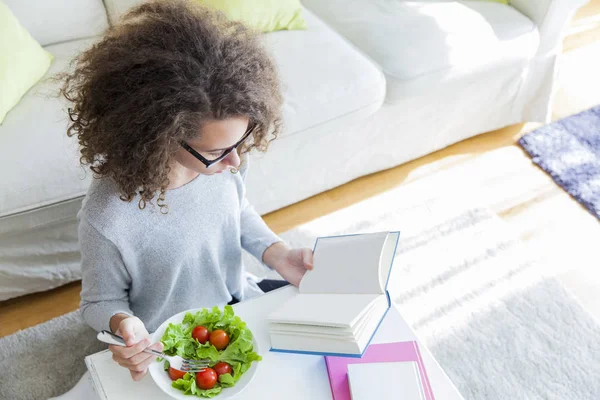 Pelo rizado adolescente chica leyendo libro y comer ensalada — Foto de Stock