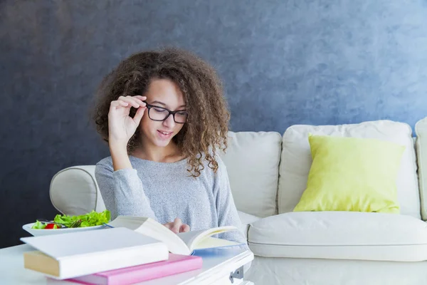 Gadis remaja rambut keriting membaca buku dan makan salad — Stok Foto