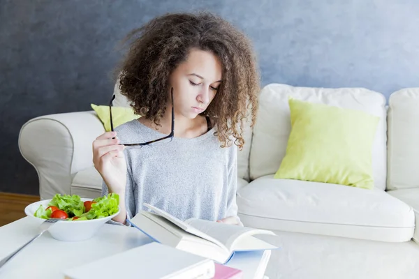 Pelo rizado adolescente chica leyendo libro y comer ensalada — Foto de Stock