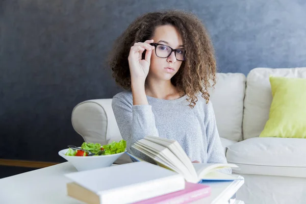 Curly hair teen girl reading book and eating salad — Stock Photo, Image