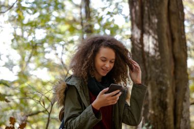 Kıvırcık saçlı genç kız ile sonbahar orman içinde smartphone