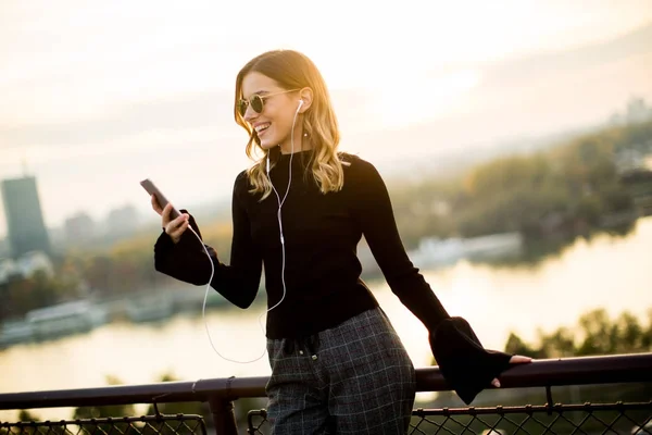 Mujer joven de moda escuchando música desde el teléfono inteligente al aire libre — Foto de Stock