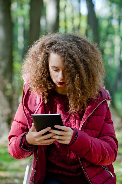 Cabello rizado chica adolescente con tableta digital en el parque de otoño — Foto de Stock