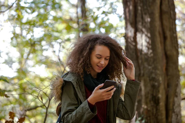 Cabello rizado chica adolescente con teléfono inteligente en el bosque de otoño — Foto de Stock