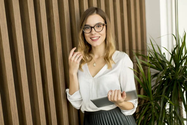 Jeune femme d'affaires avec tablette par mur dans un bureau moderne — Photo