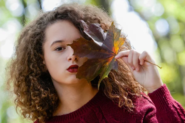 Lockiges Haar Teenie-Mädchen hält Ahornblatt im Herbstwald — Stockfoto
