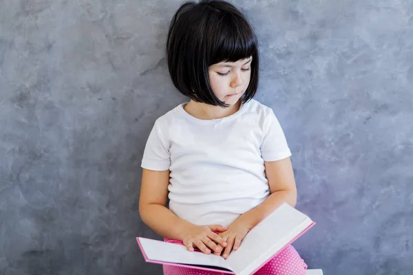 Mignon noir cheveux petite fille lecture livre par le mur — Photo