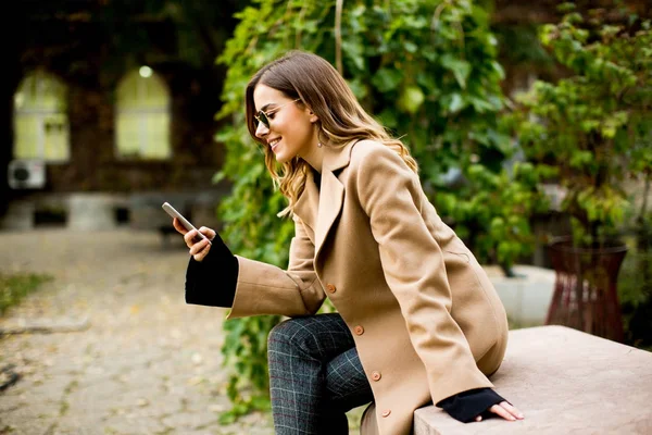 휴대 전화를 사용 하 여 야외에 앉아 젊은 여자 — 스톡 사진