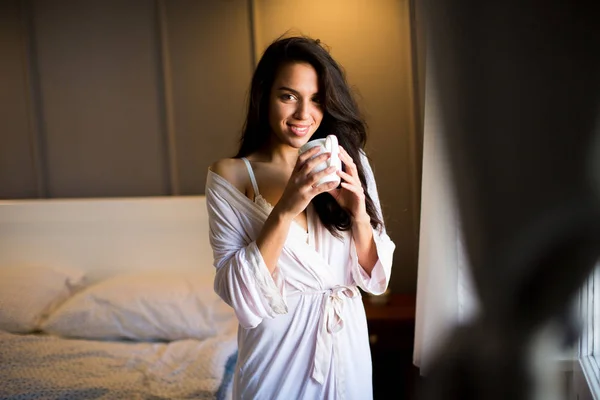 Mujer joven con taza en el dormitorio — Foto de Stock