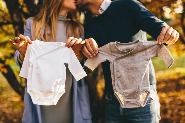 Schwangere Frau und ihr Mann mit Kleidung für Neugeborene — Stockfoto