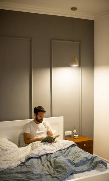 Jovem homem lendo livro na cama — Fotografia de Stock