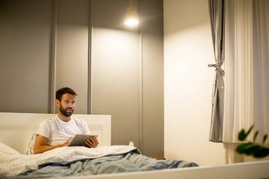 Genç adam yatakta yatarken dijital tablet kullanma