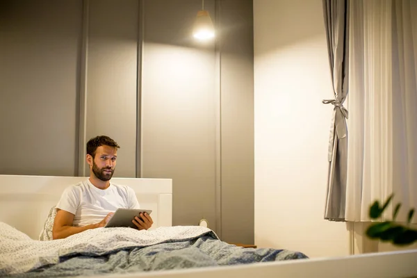 Молодий чоловік, використовуючи цифровий планшет, лежить на ліжку — стокове фото