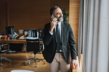 cep telefonu kullanarak modern ofisinde kıdemli işadamı portresi