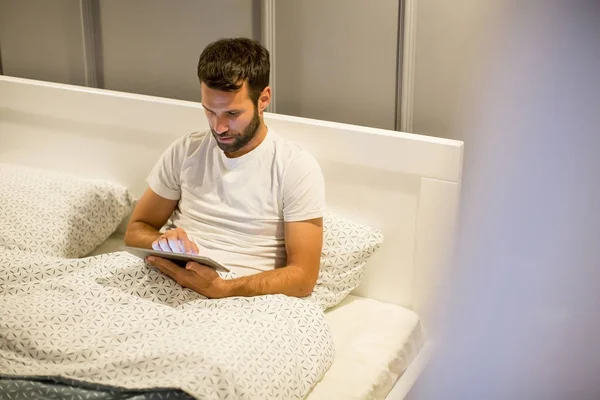Hombre joven usando tableta digital acostado en la cama — Foto de Stock