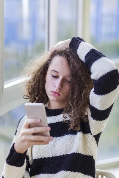 Σγουρά μαλλιά κορίτσι με κινητό τηλέφωνο από το παράθυρο — Φωτογραφία Αρχείου