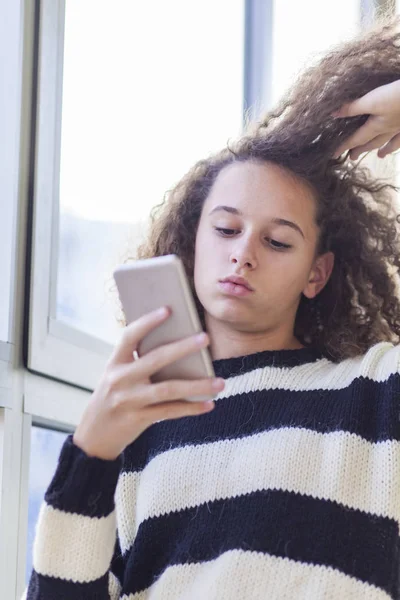 Σγουρά μαλλιά κορίτσι με κινητό τηλέφωνο από το παράθυρο — Φωτογραφία Αρχείου