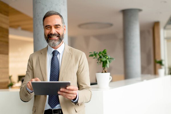 Портрет красивого зрелого бизнесмена с цифровым планшетом в офисе
