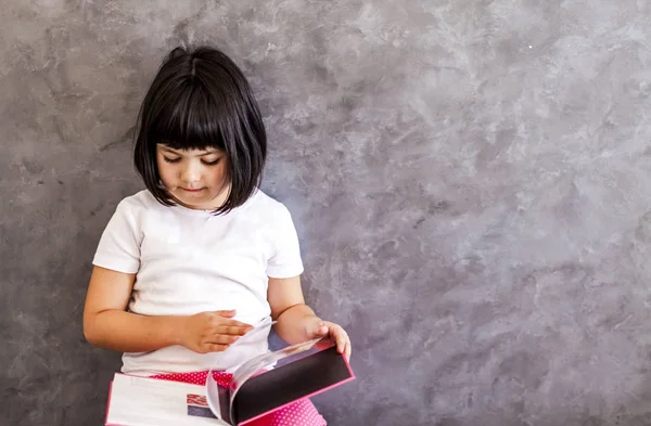 Little girl reading book by the wall — Stock Photo, Image