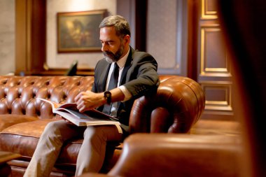 Yakışıklı orta yaşlı işadamı kanepede kitap okuma