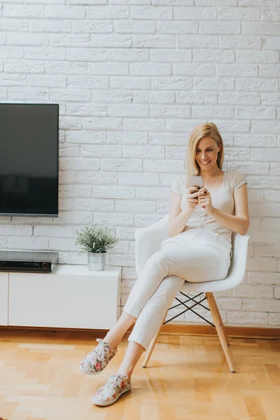 Giovane donna seduta nella stanza e utilizzando il telefono — Foto Stock