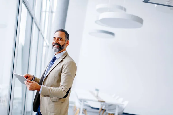 Knappe rijpe zakenman met digitale tablet in het kantoor — Stockfoto