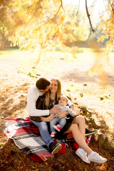 Jovem família sentada no chão no parque de outono — Fotografia de Stock