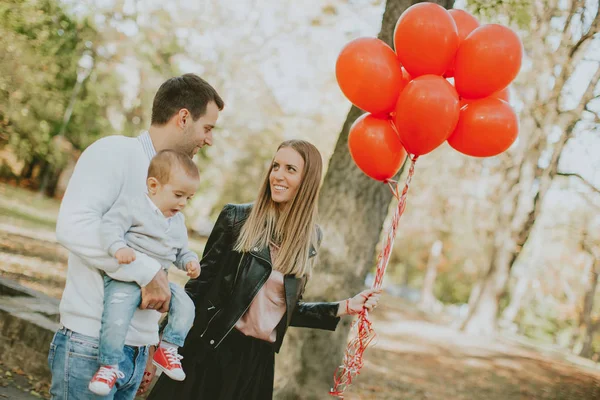 Happy young parents with baby boy in autumn park holding red bal