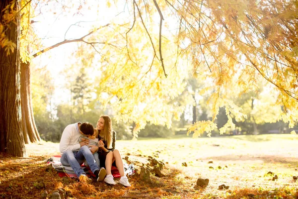 Nuori perhe istuu maassa syksyllä puistossa — kuvapankkivalokuva
