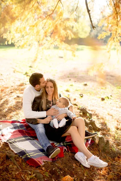 Jovem família sentada no chão no parque de outono — Fotografia de Stock