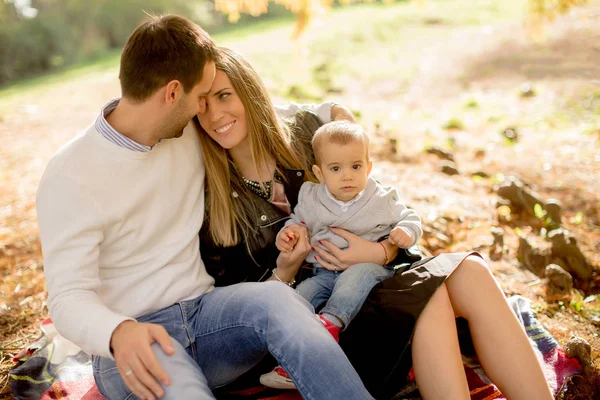 Young family sitting on the ground in autumn park — Stock Photo, Image