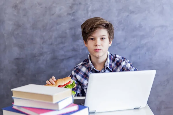 Adolescente chico come un sándwich y web-surf — Foto de Stock