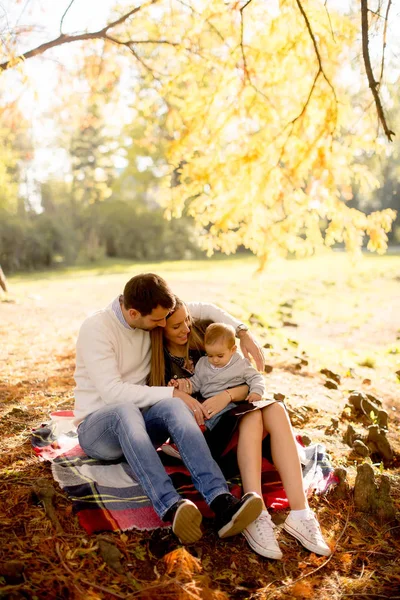 Familia joven sentada en el suelo en el parque de otoño — Foto de Stock