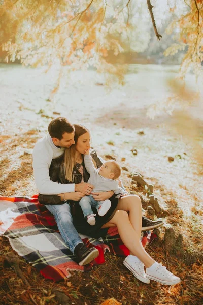 Jeune famille assise sur le sol dans le parc d'automne — Photo