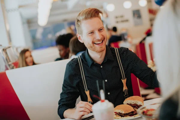 Joven comiendo hamburguesa con queso en la cafetería — Foto de Stock