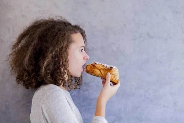 Tiener meisje krullend haar eten croissant — Stockfoto